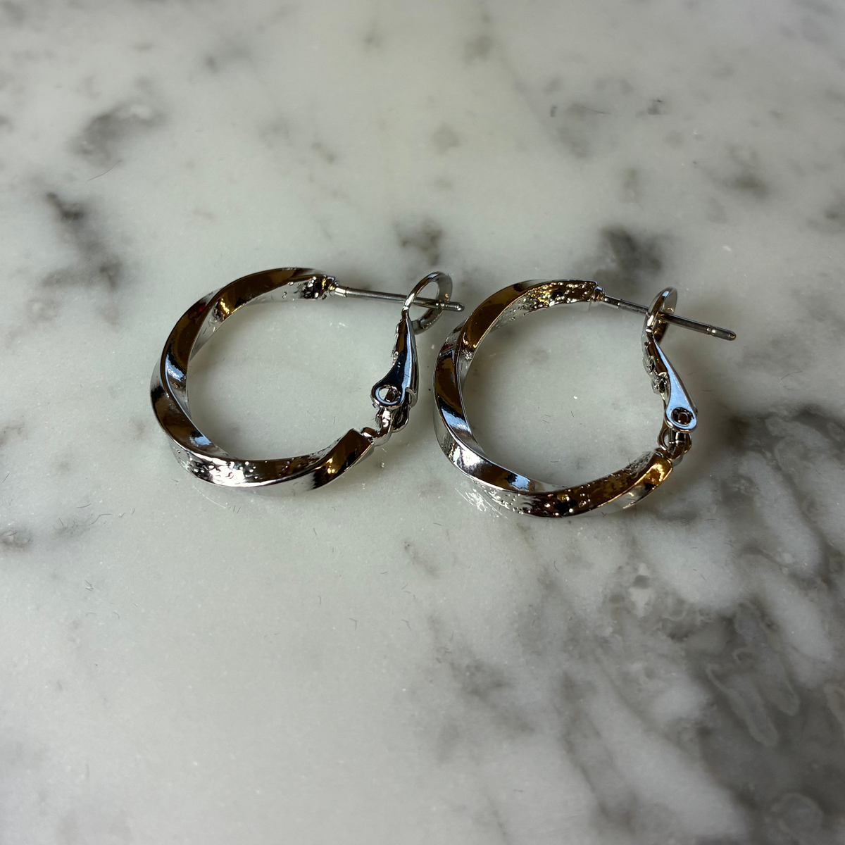 Small textured twist hoop earring by MX, close-up view showing detailed, shiny silver hoop with textured surface.