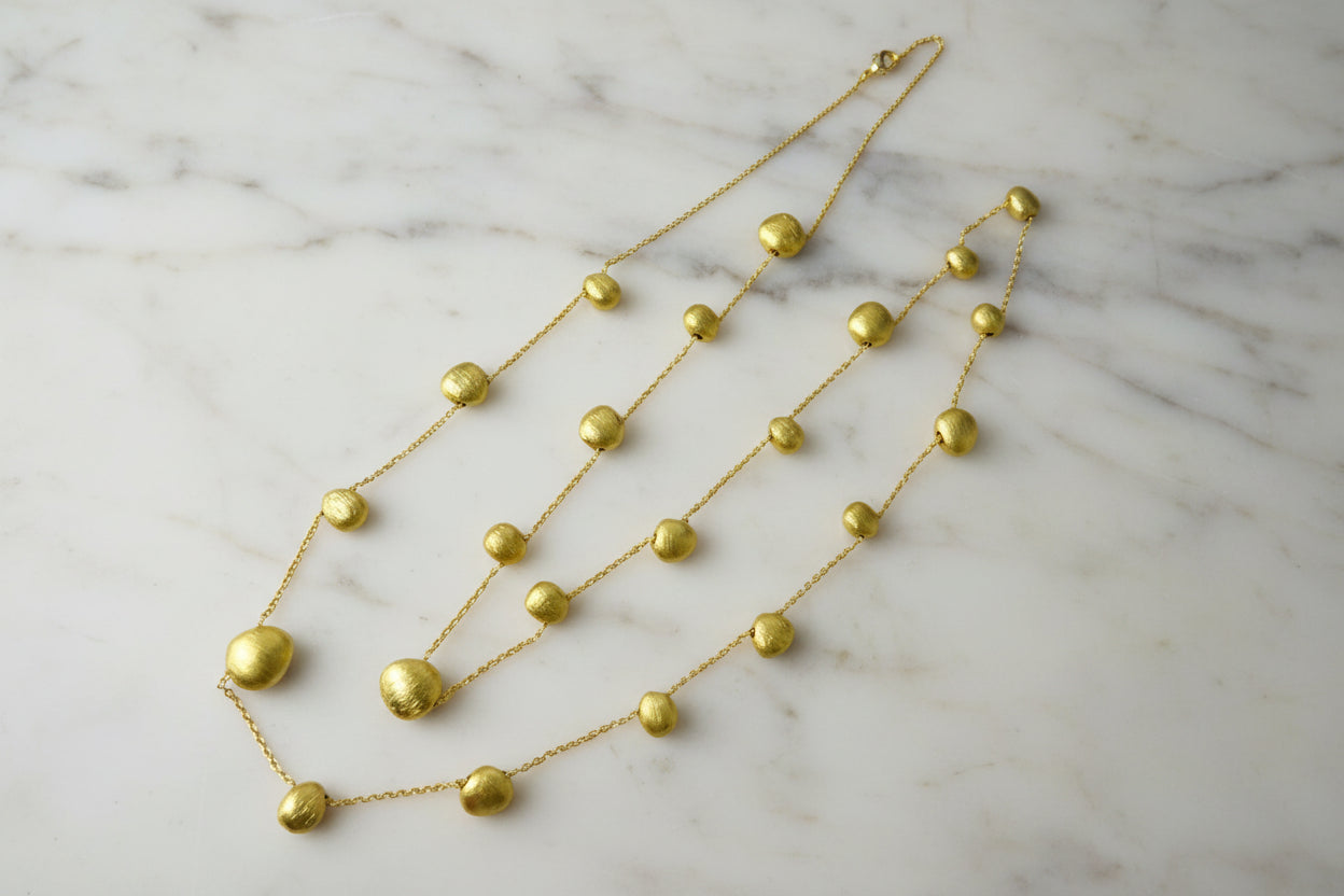 Lorena brushed gold bead necklace featuring smooth gold beads on a delicate chain, showcasing elegant jewelry design.