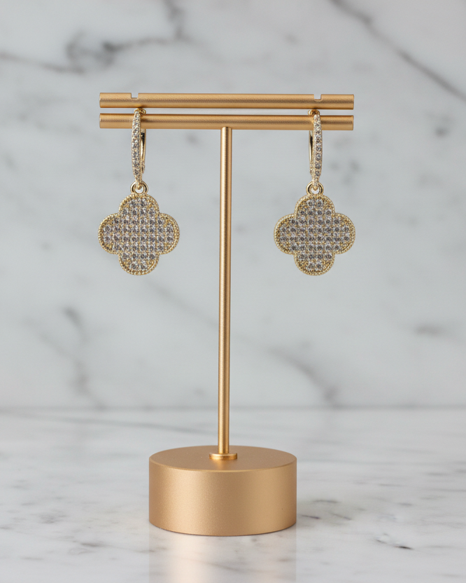 Lorena pave hoop earring with a dangling clover-shaped charm, showcasing shiny metal and intricate detailing.